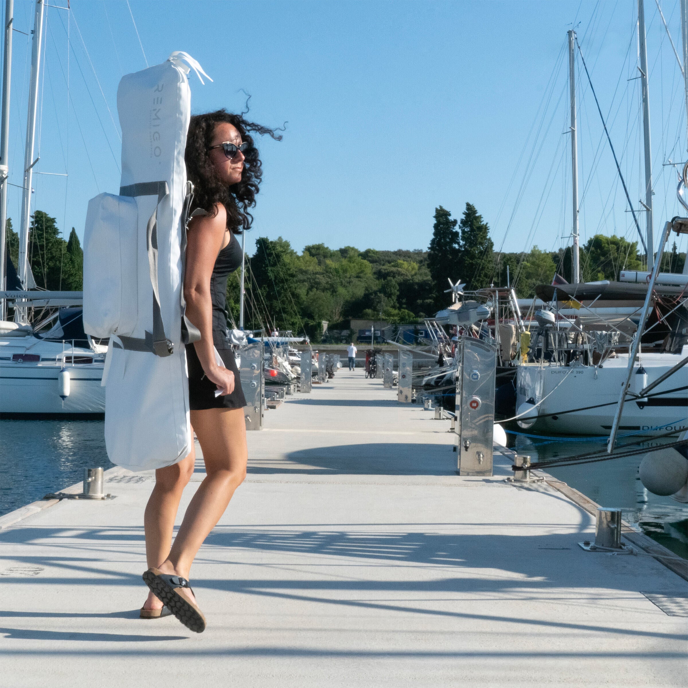 Woman holding a large white bag on a dock with boats in the background