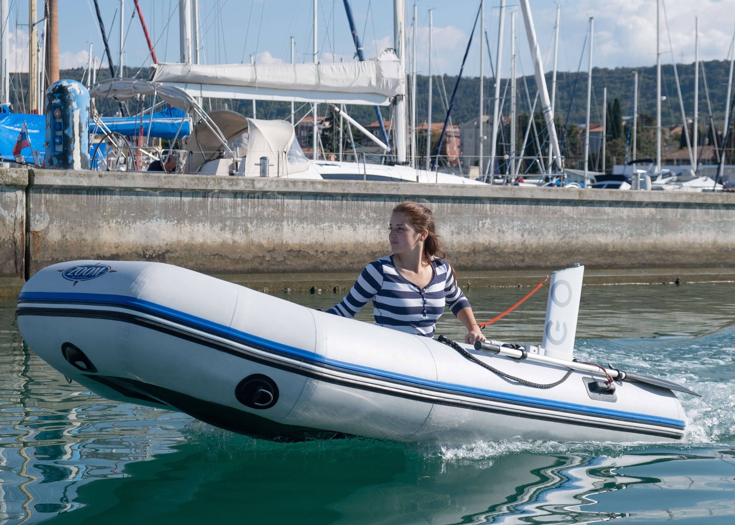 Woman steering an inflatable boat on water with a marina in the background with Remigo electric outboard
