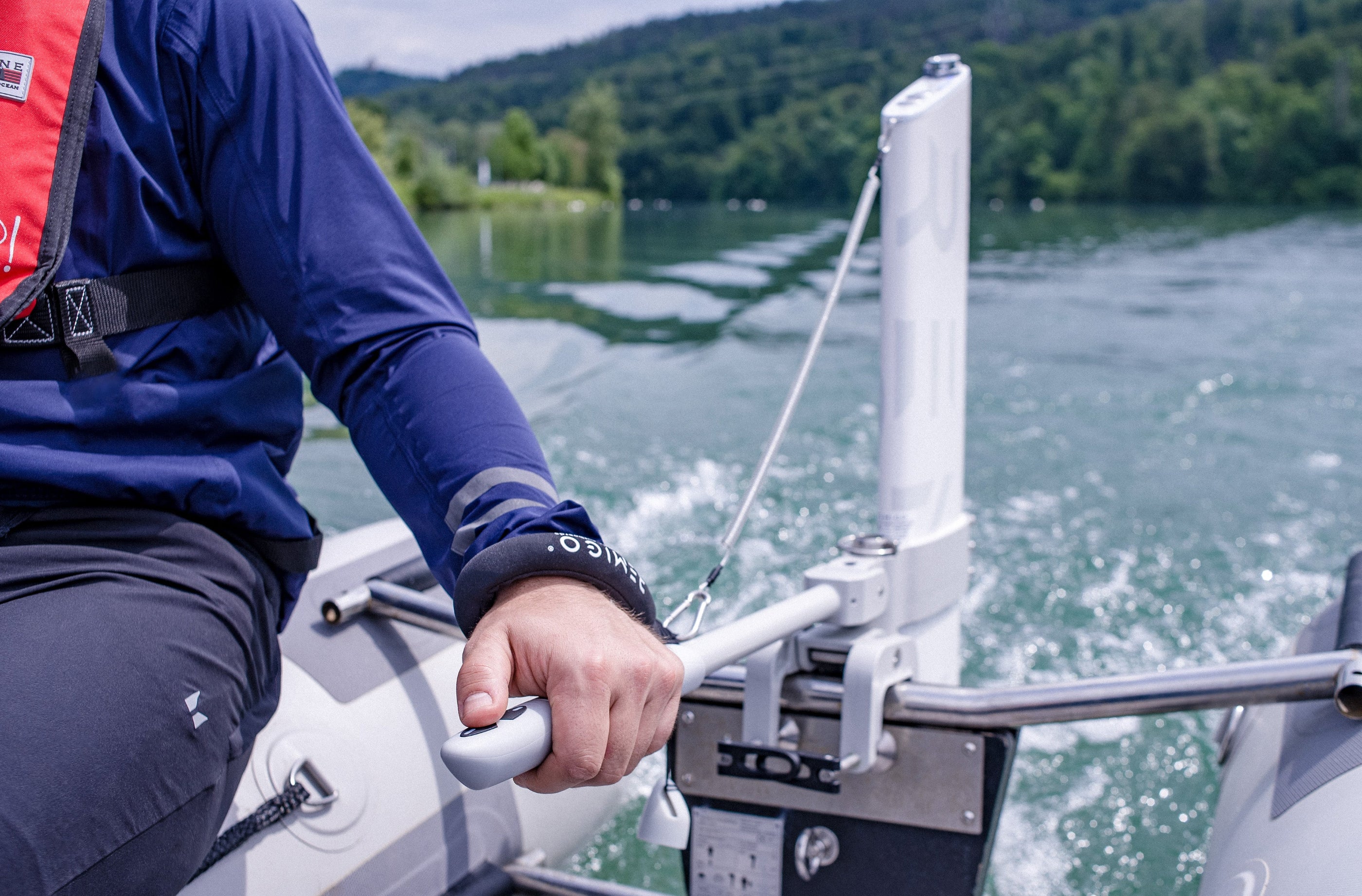 Person on a boat holding onto a handle with remote control key with a scenic lake and trees in the background