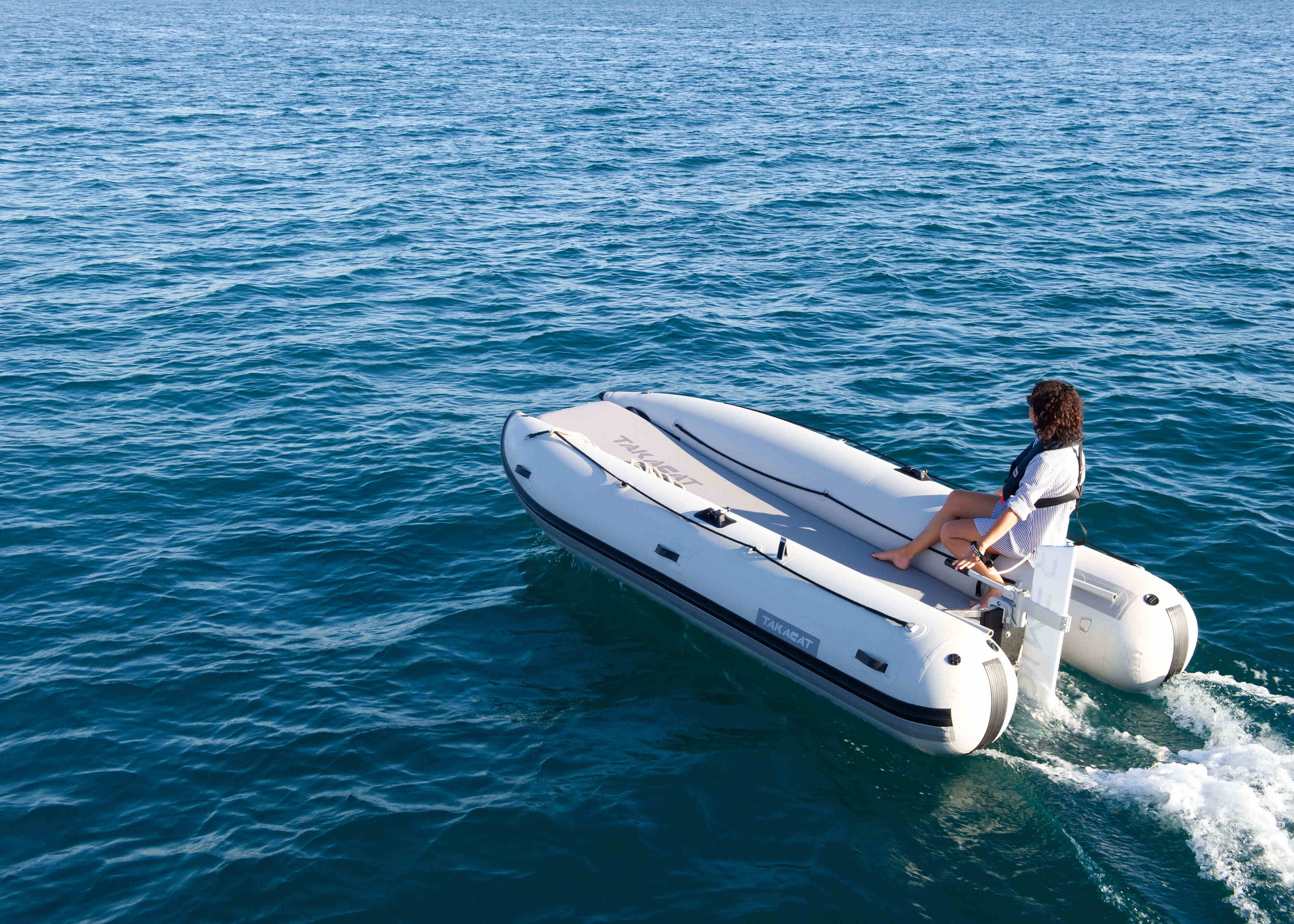 Person on a white inflatable boat in the ocean holding Remigo electric engine