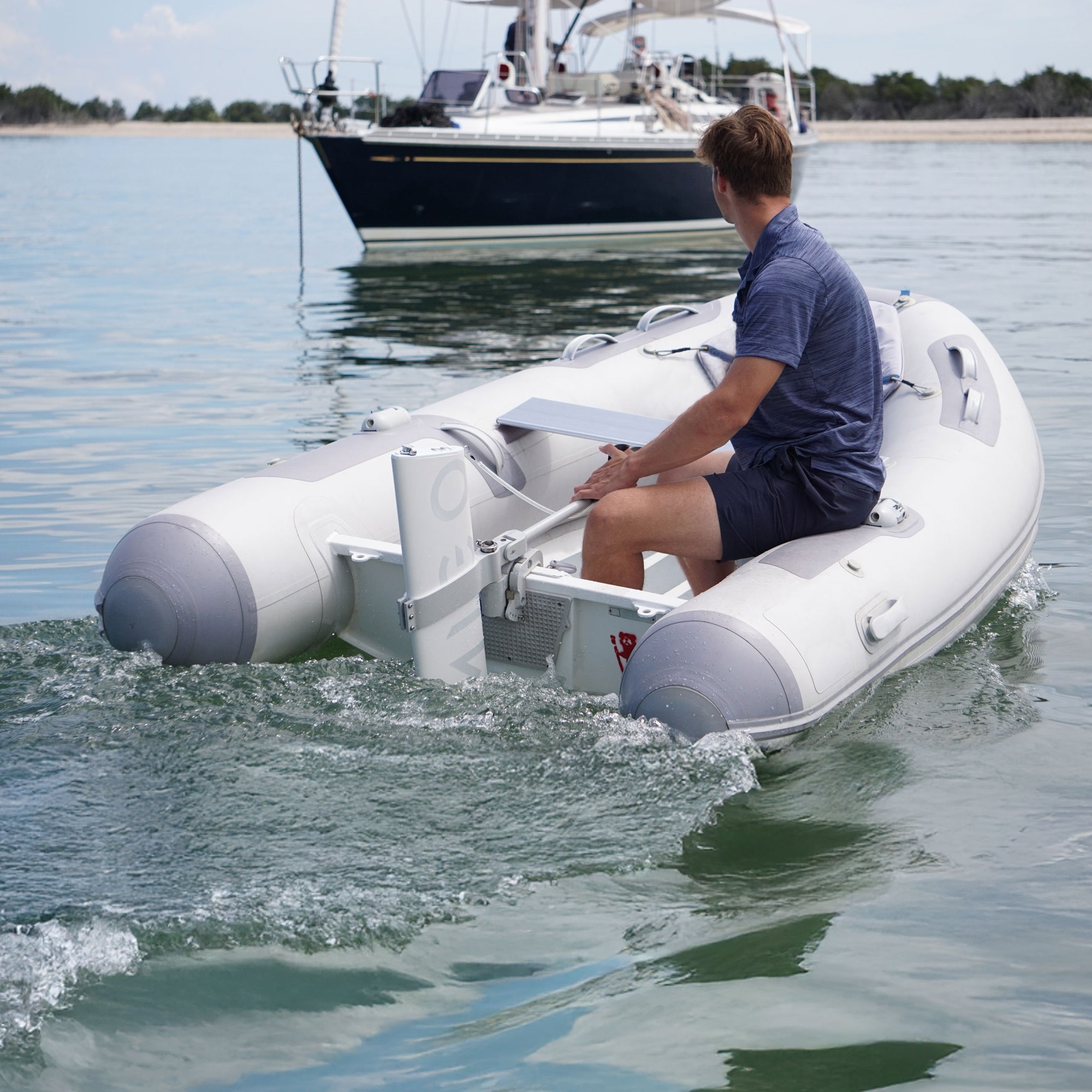 Person on an inflatable boat in the water with another boat in the background.