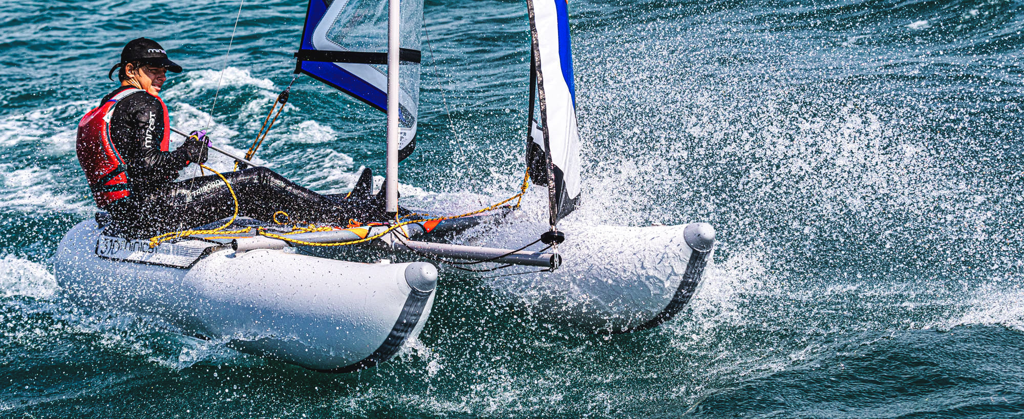 MiniCat model 310 Sport with blue sails sailing fast on the sea with a young boy sailing it