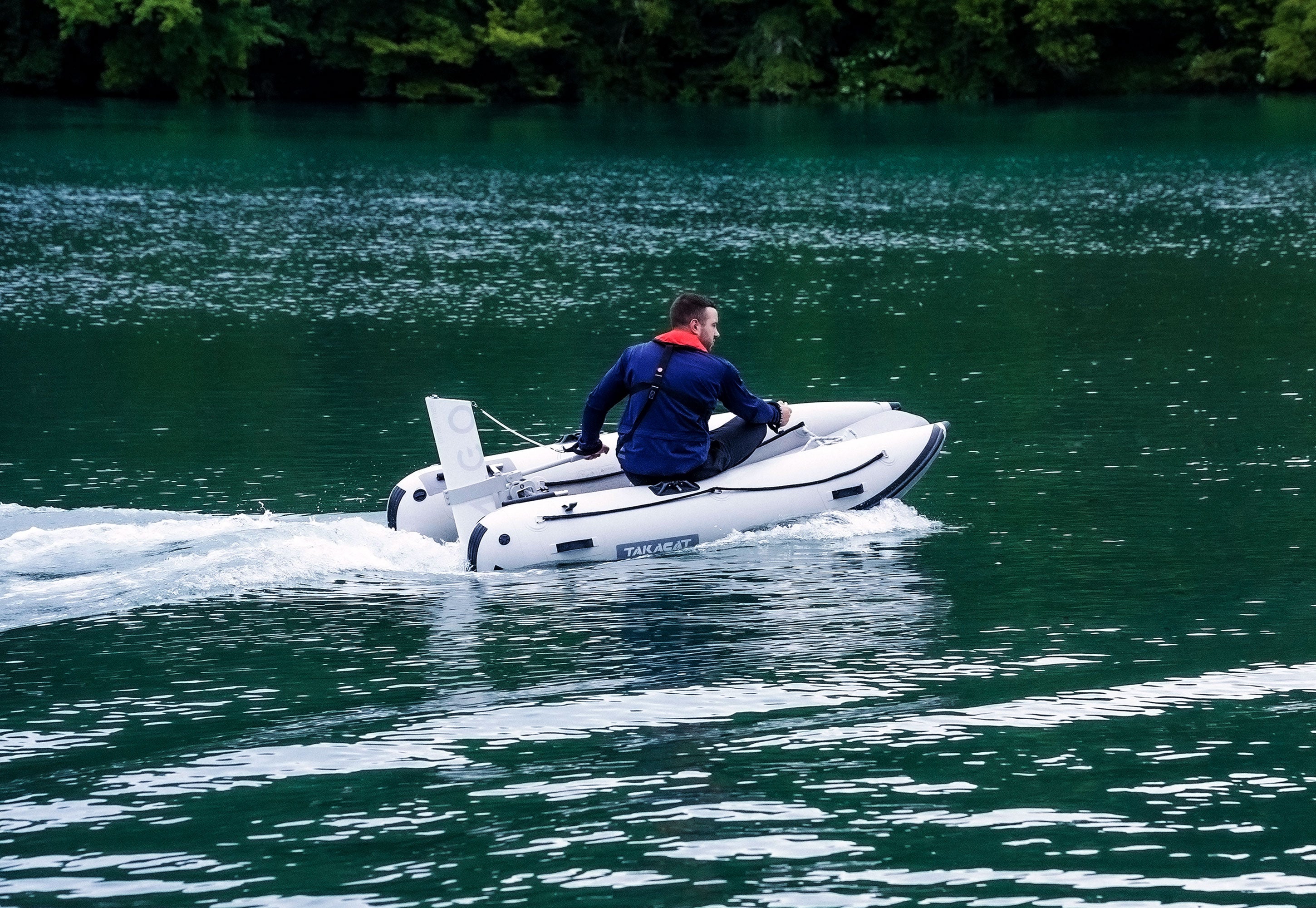Person on a small inflatable boat in a body of water with trees in the background
