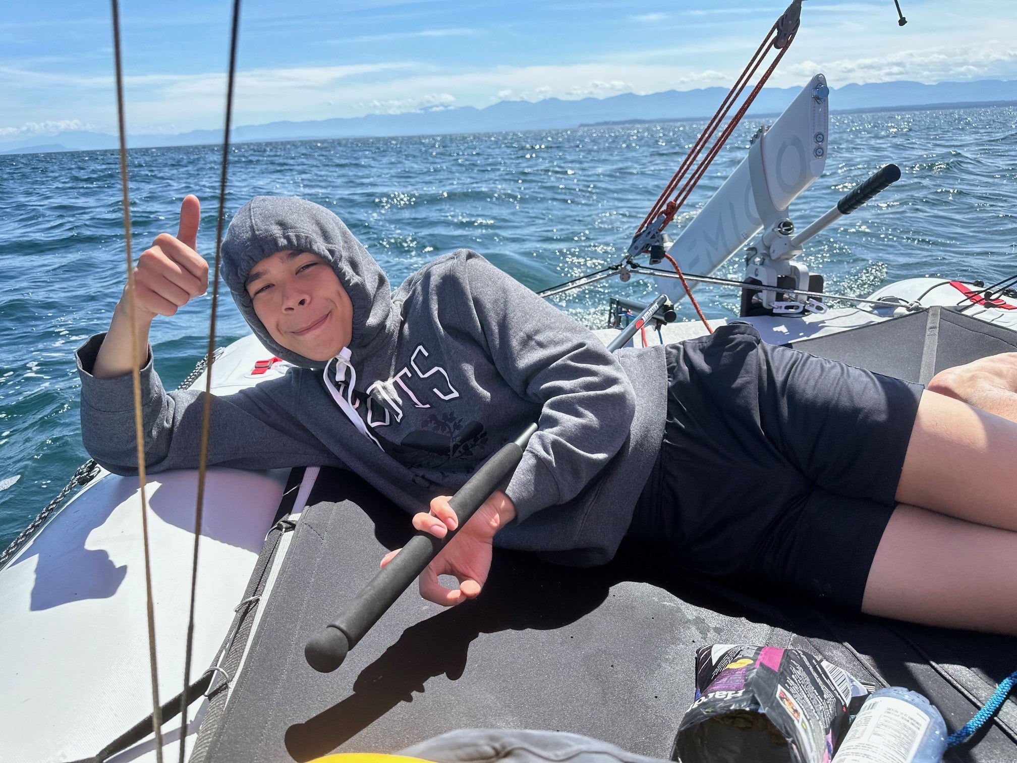 Person on a sailboat MiniCat 520 Explorer giving a thumbs-up with a scenic ocean background