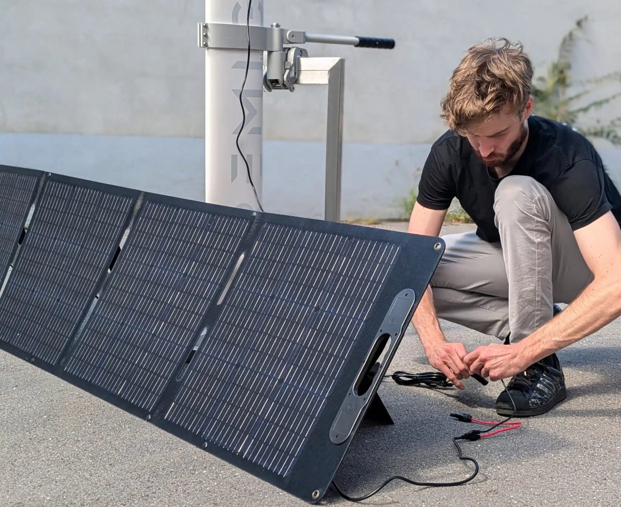 Person setting up a solar panel on the ground with a concrete wall in the background