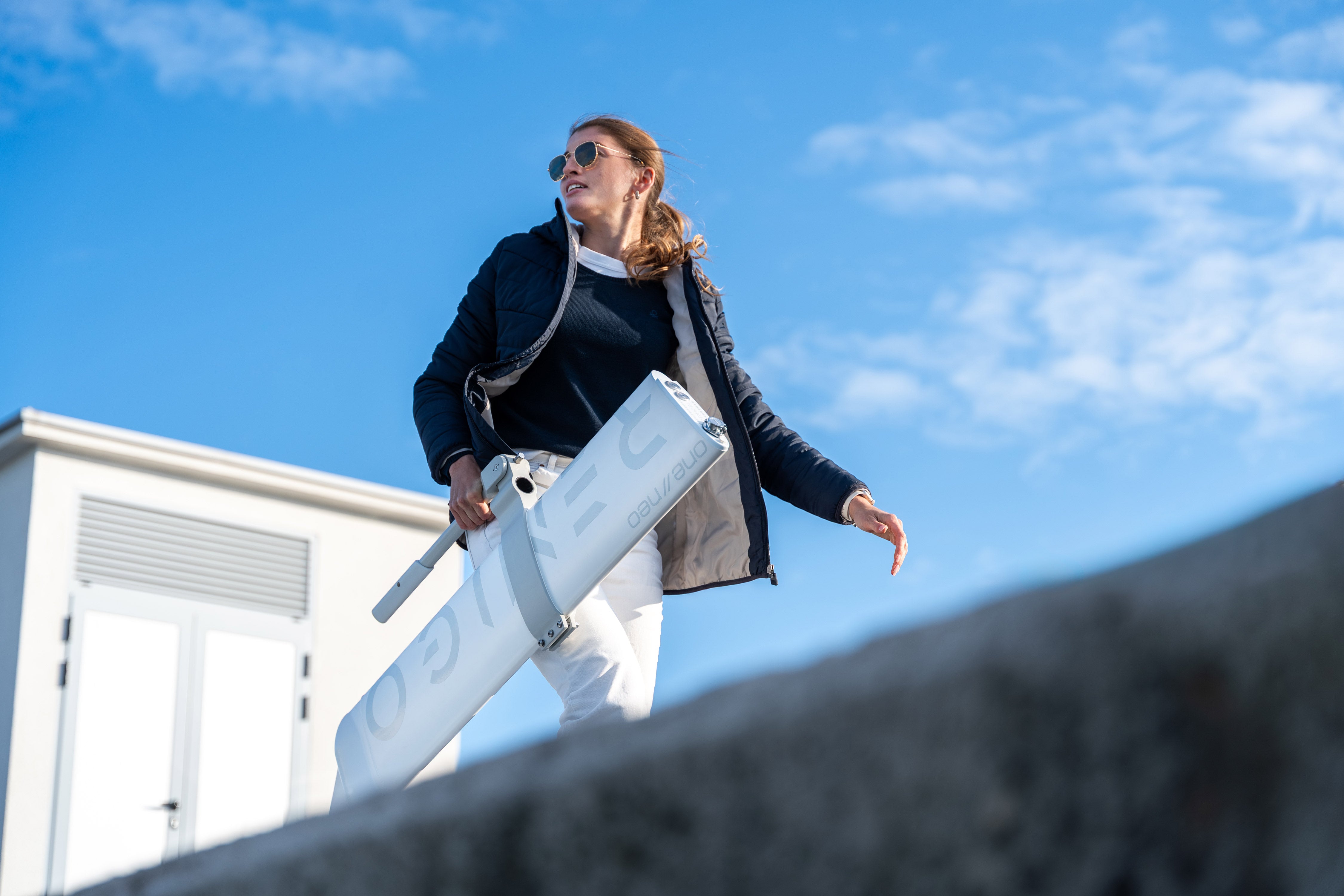 Woman holding a white suitcase against a blue sky with a building in the background
