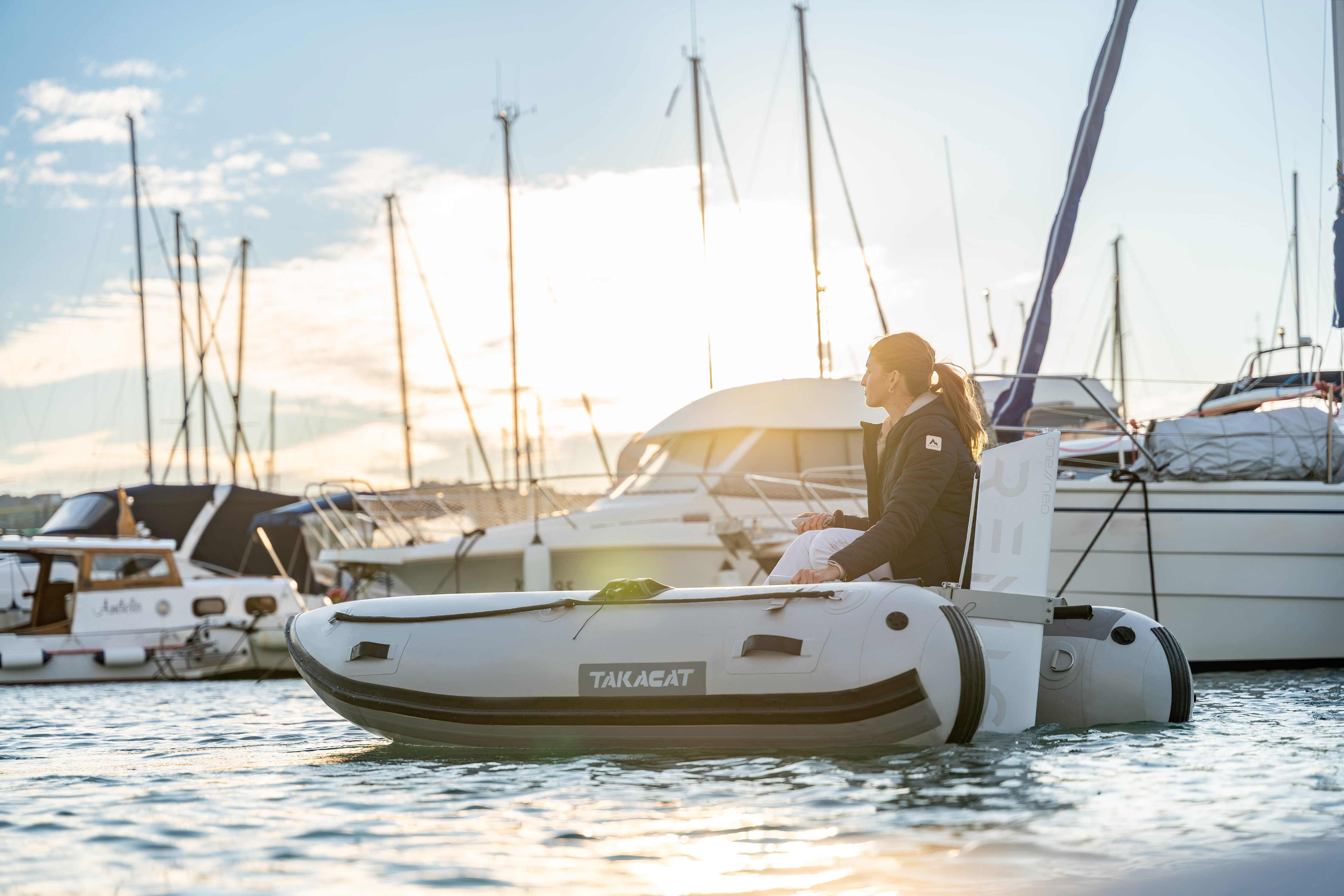Person on a Takacat inflatable boat in a marina with sailboats.