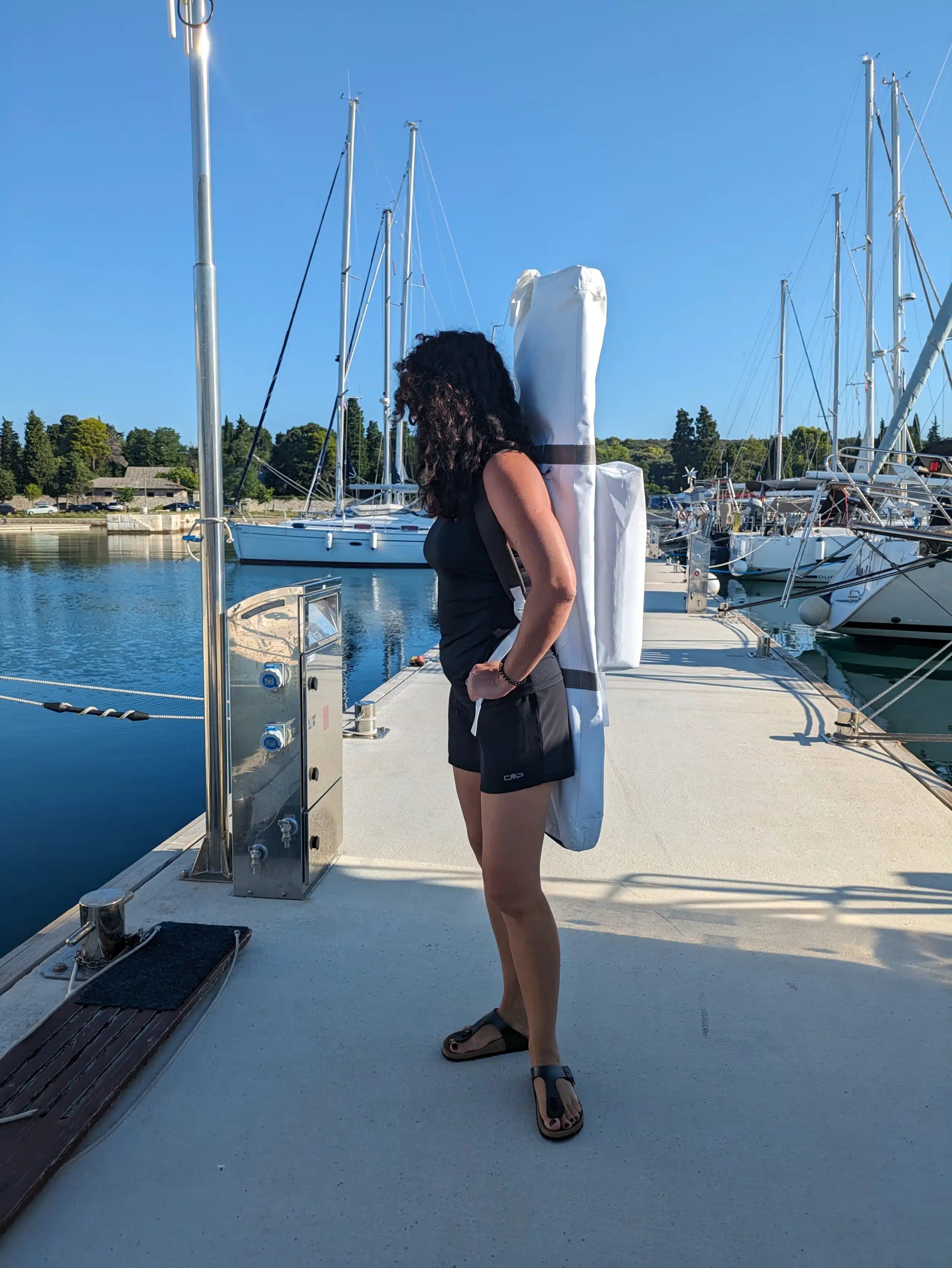 Person standing on a boat holding a white sail with a marina in the background