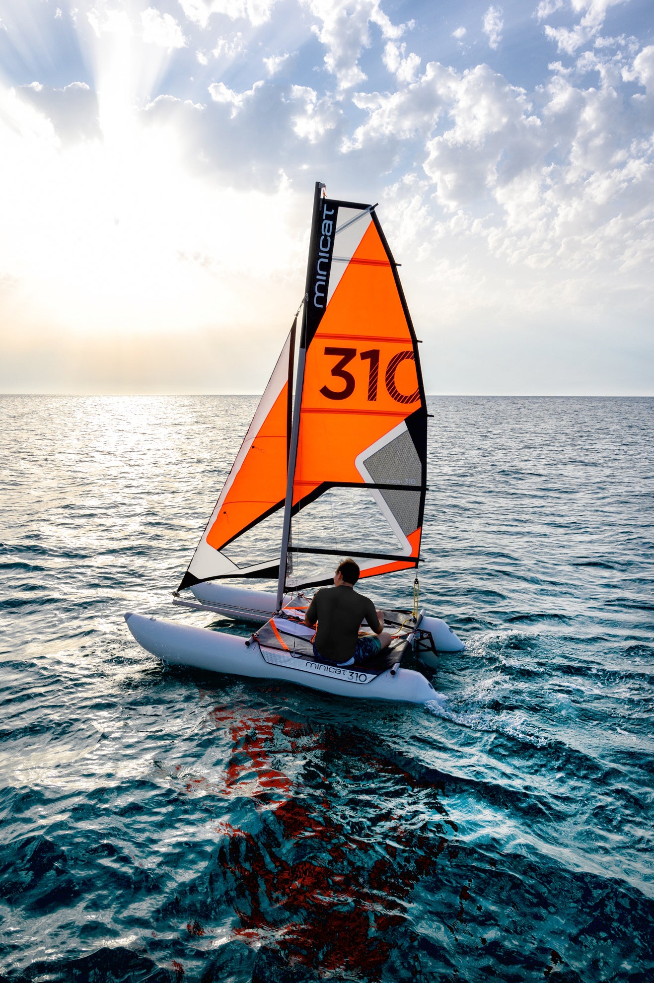 Person sailing on a small boat MiniCat with an orange sail labeled '310' on a calm sea.