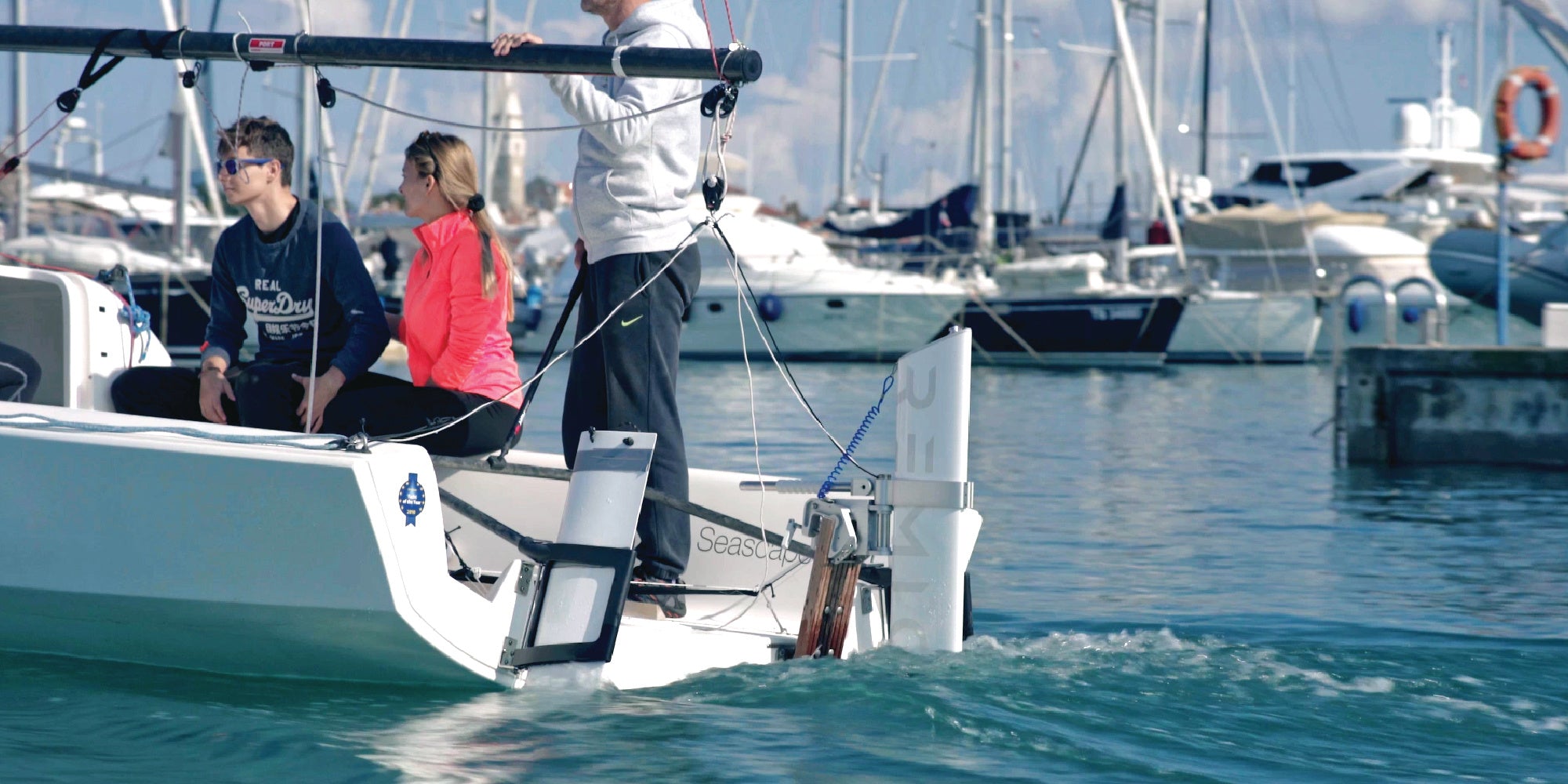 People on a sailboat in a harbor with other boats in the background