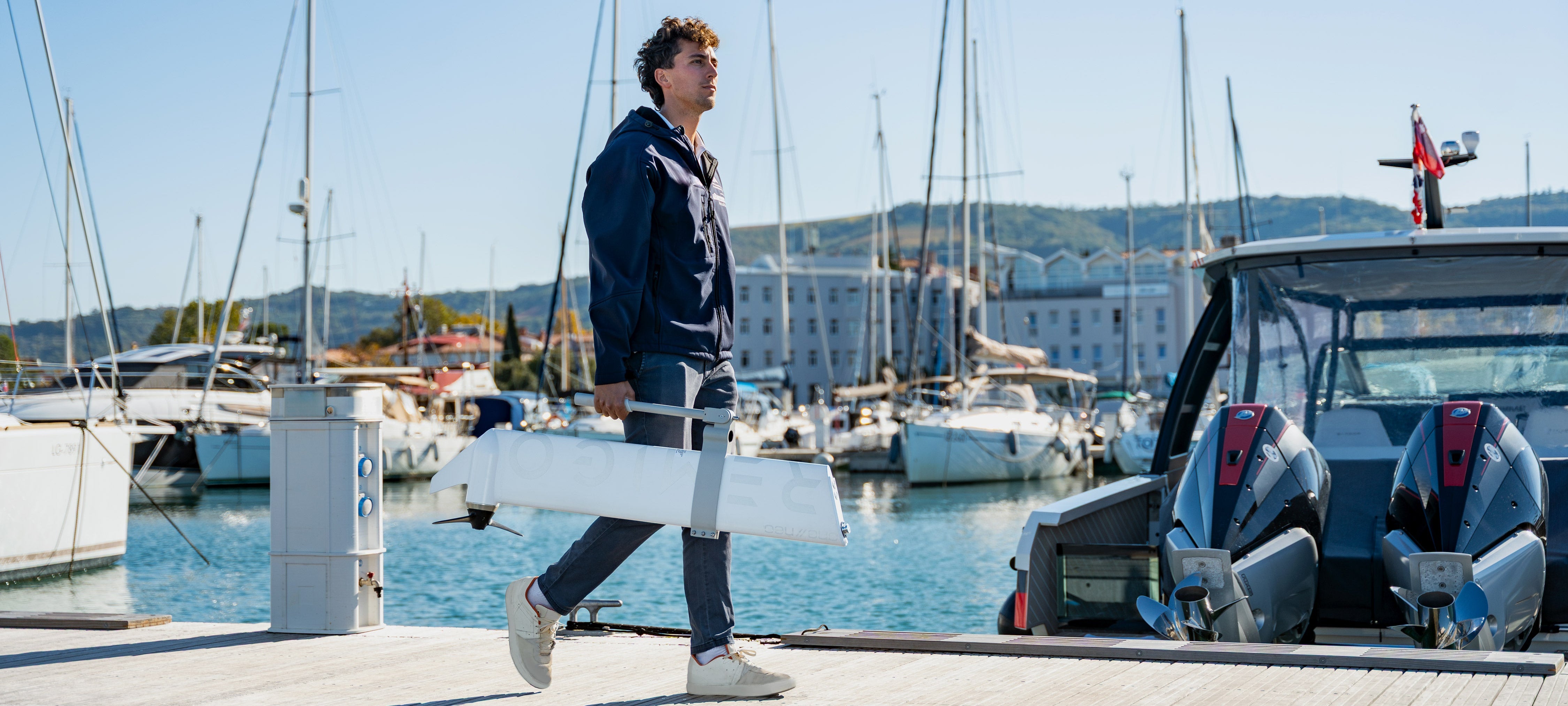 Person holding Remigo Electric outboard in a marina with boats and clear sky