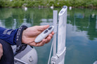 Hand holding a remote control near a boat with water in the background