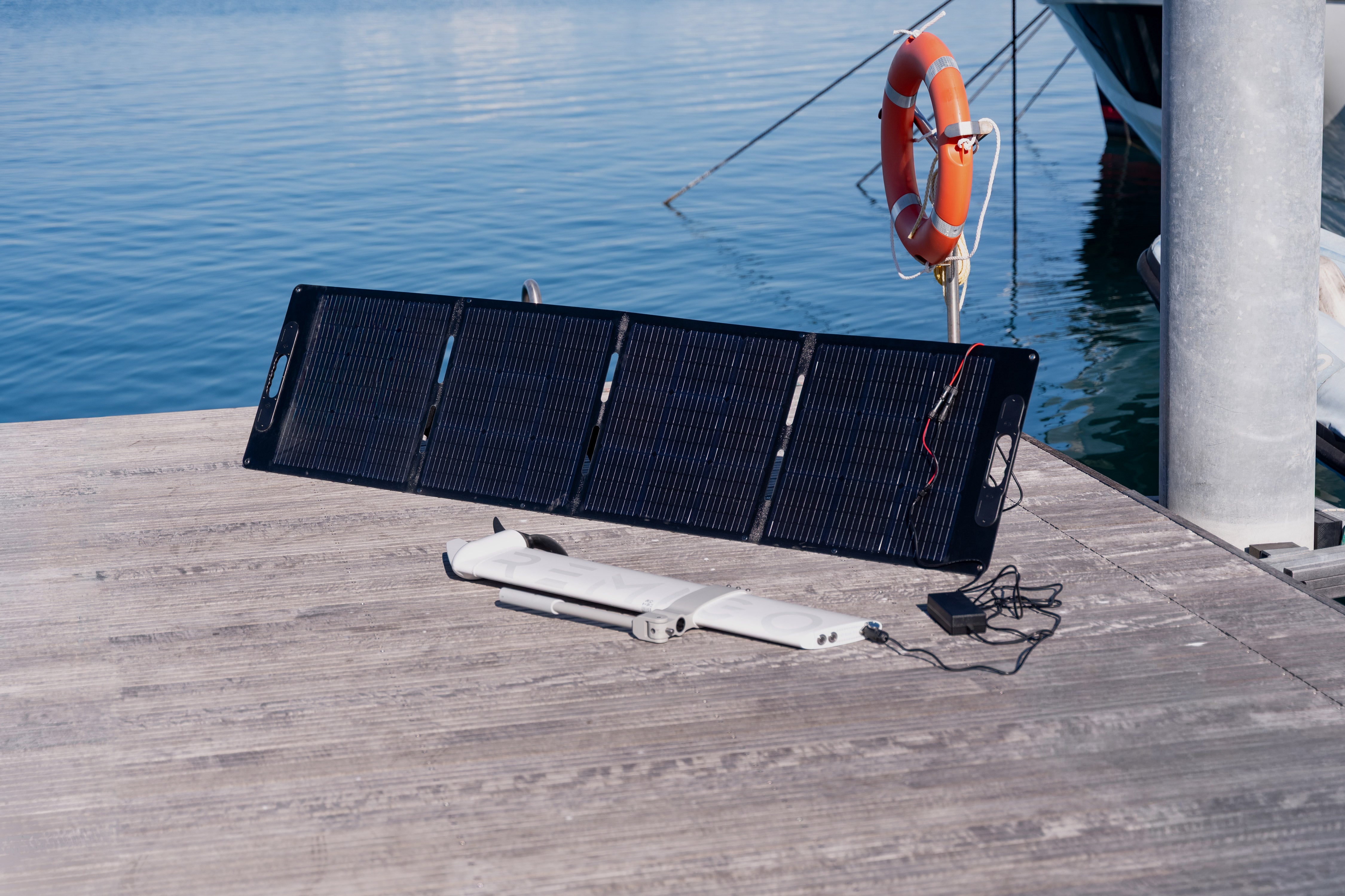 Foldable solar panel on a dock by a body of water with a life buoy in the background.