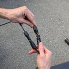 Two hands holding black electrical connectors against a gray pavement background