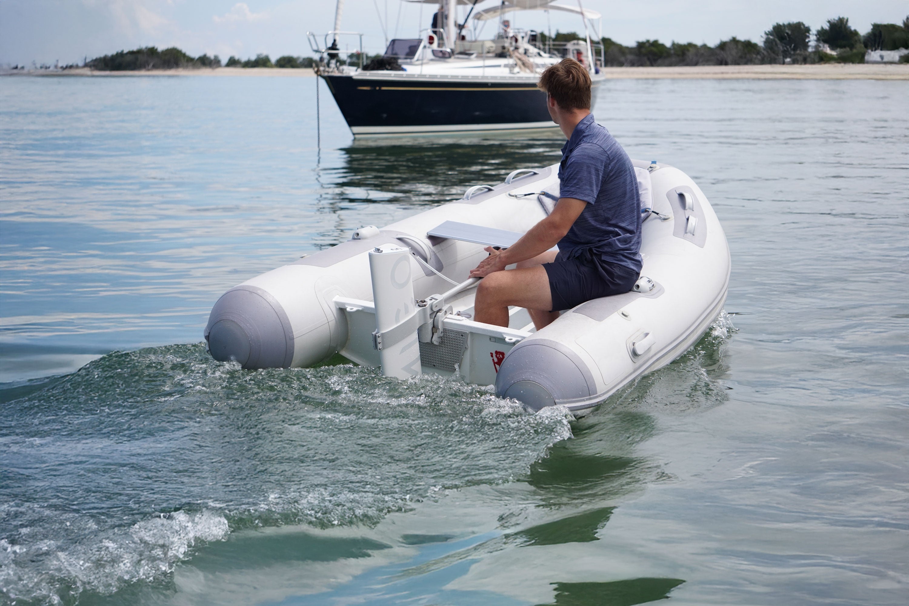 Person on an inflatable boat in the water with another boat in the background.