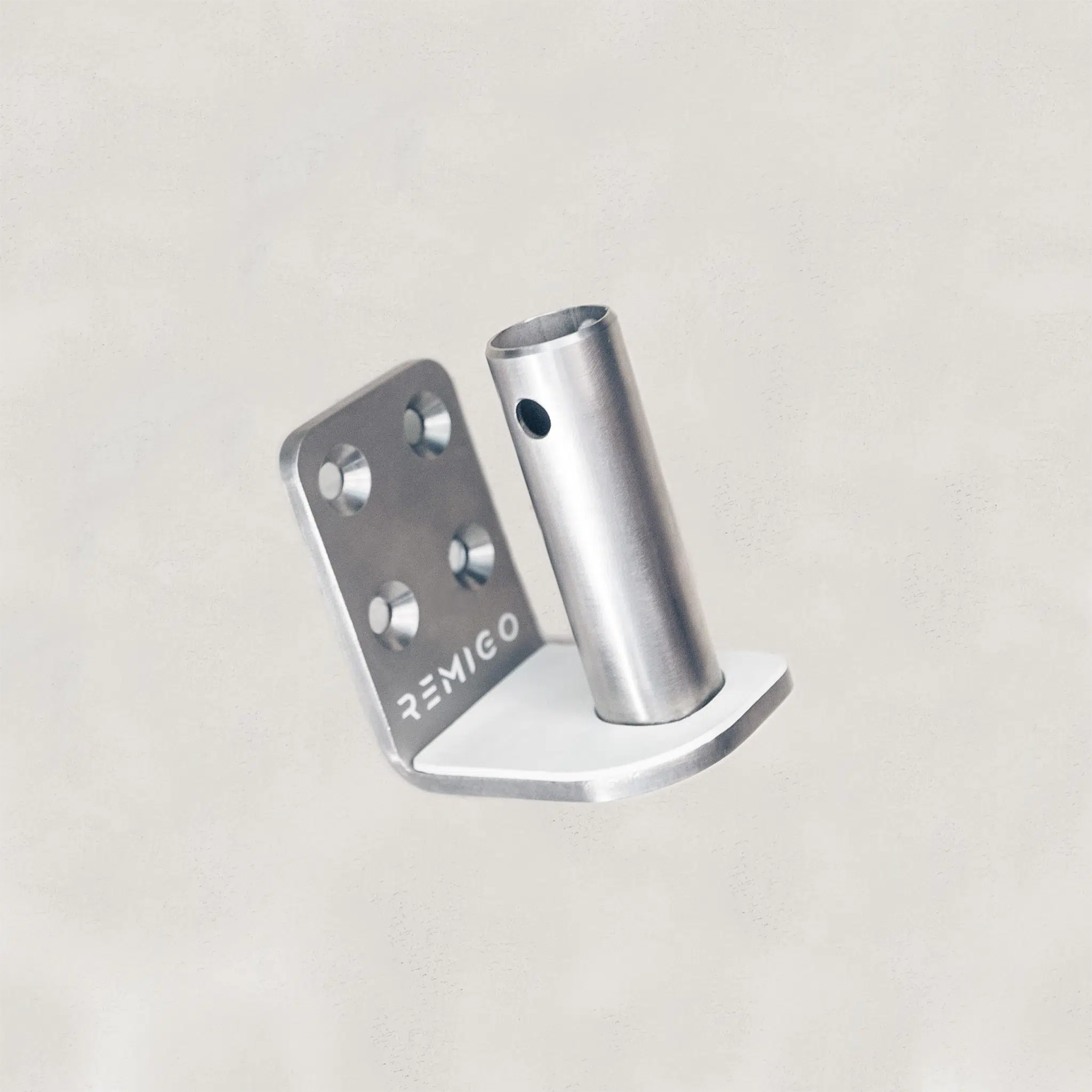 Metal bracket with cylindrical component on a light gray background, featuring the brand 'REMIGO'.